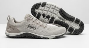 A pair of light grey Xero Shoes with branding on the side; one shoe is upright, the other on its side displays a black and white textured sole—designed for walking and all-day comfort with a visible tread pattern.