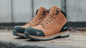 A pair of tan and black Xero Shoes, renowned for their comfort as work boots, rest on a concrete surface with a blurred background.