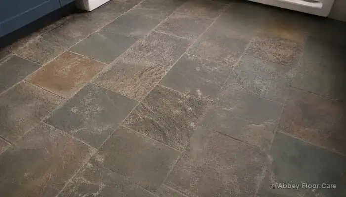 Dull riven slate floor in a UK kitchen showing residue trapped in grout joints and flat grey surface before cleaning