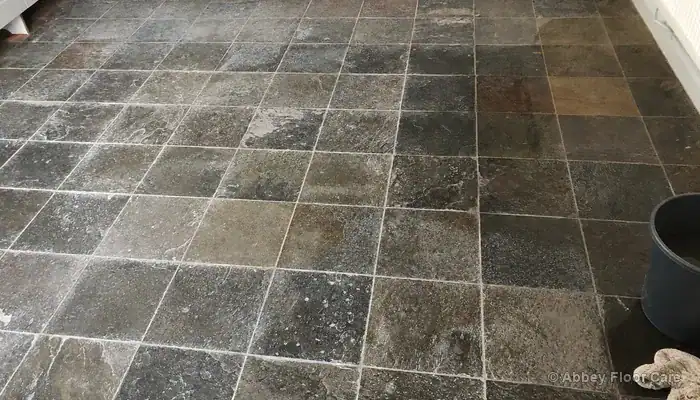 Riven slate floor mid-clean showing pale smears and uneven drying where slurry has dried back into the surface